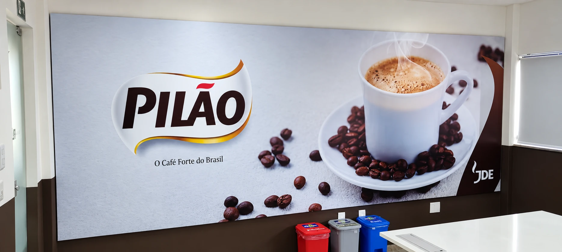 Painel panorâmico com xícara e grãos de café instalado em ambiente interno.